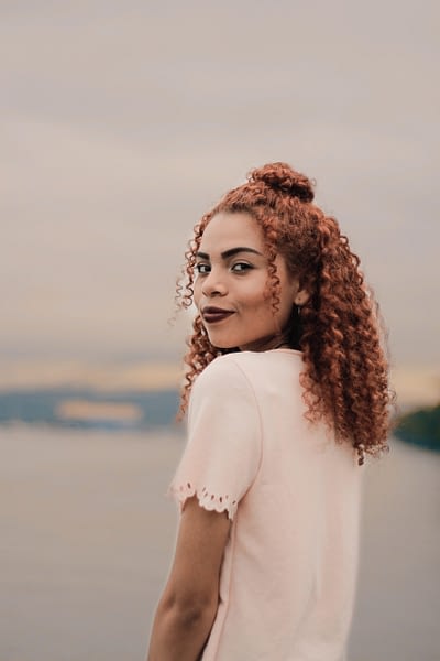 woman with curly hair standing outside in front of a lake