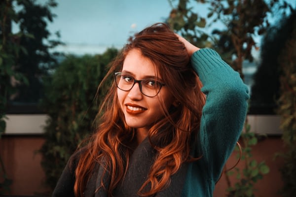 woman with red hair wearing glasses brushing her hair out of her face