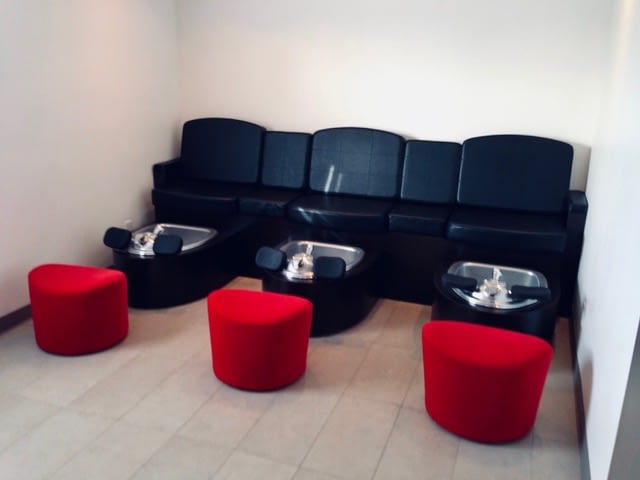 Pedicure stations with black leather seats and red foot stools