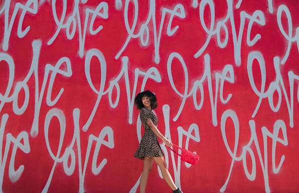woman in leopard print dress standing in front of a red wall mural that says "love"