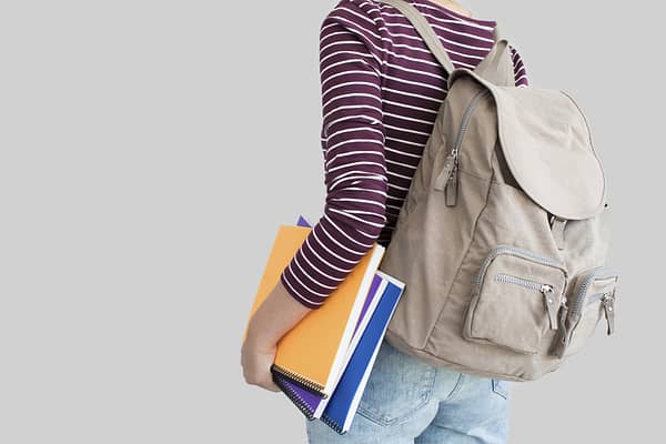 woman wearing backpack holding a stack of notebooks