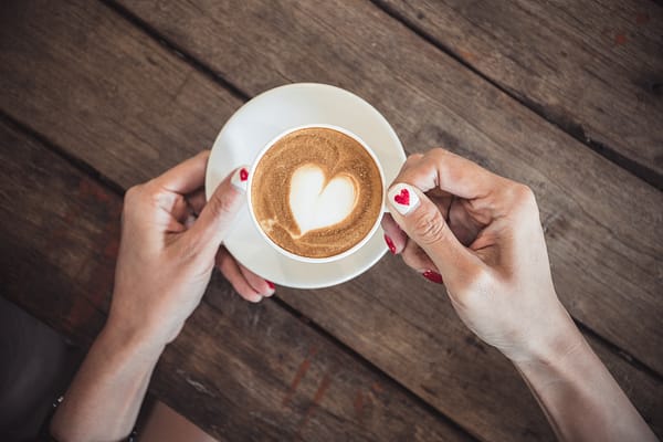 woman's hands with heart painted fingernails holding a cup of coffee