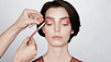 Dark haired woman getting natural makeup applied. Color swatch is displayed.