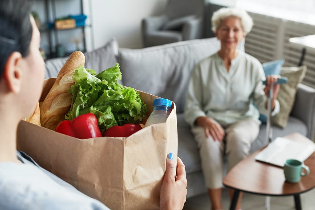 Caregiver delivering bag of groceries to smiling client at their home