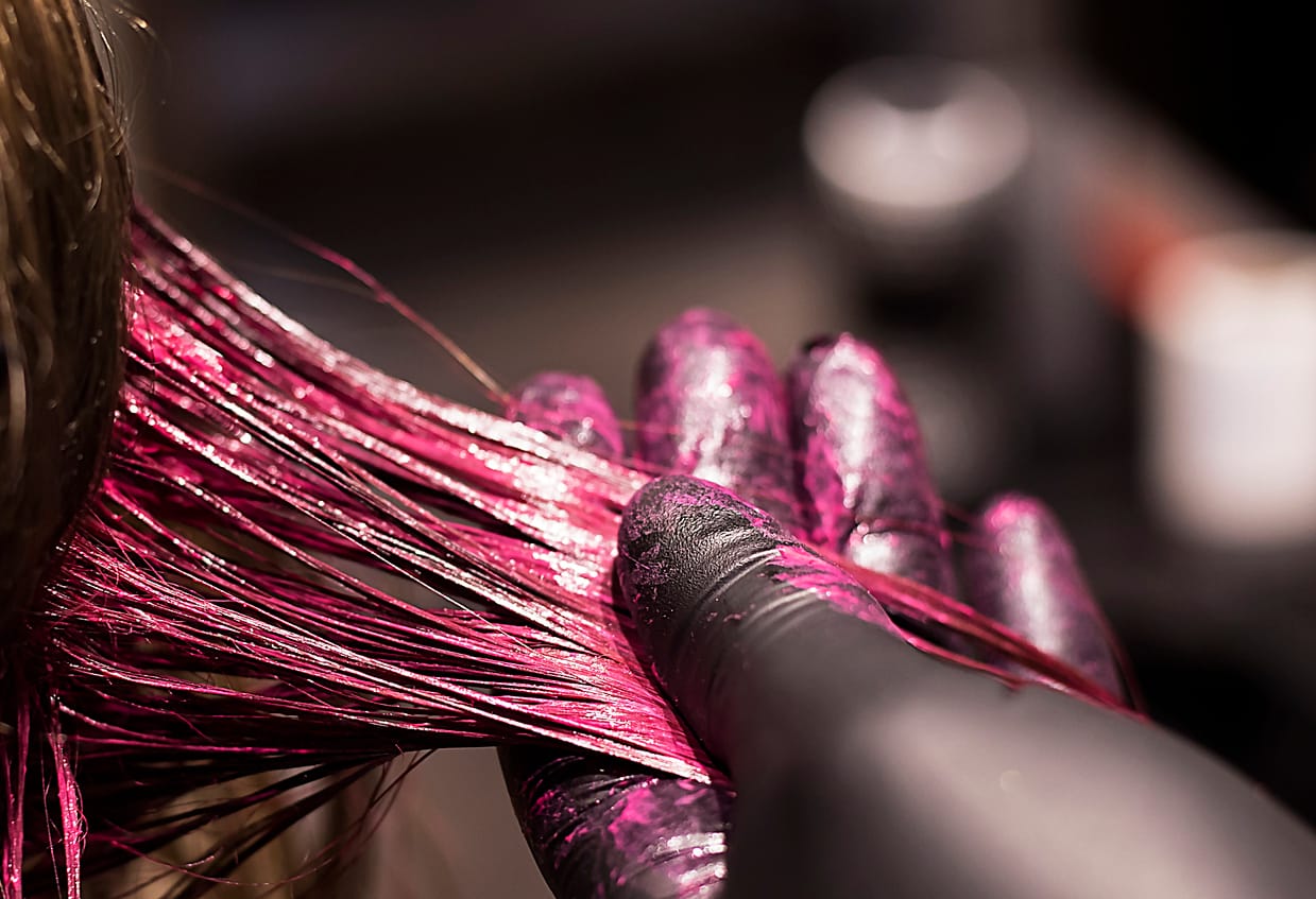 Close-up of stylist coloring strand of hair in bright pink