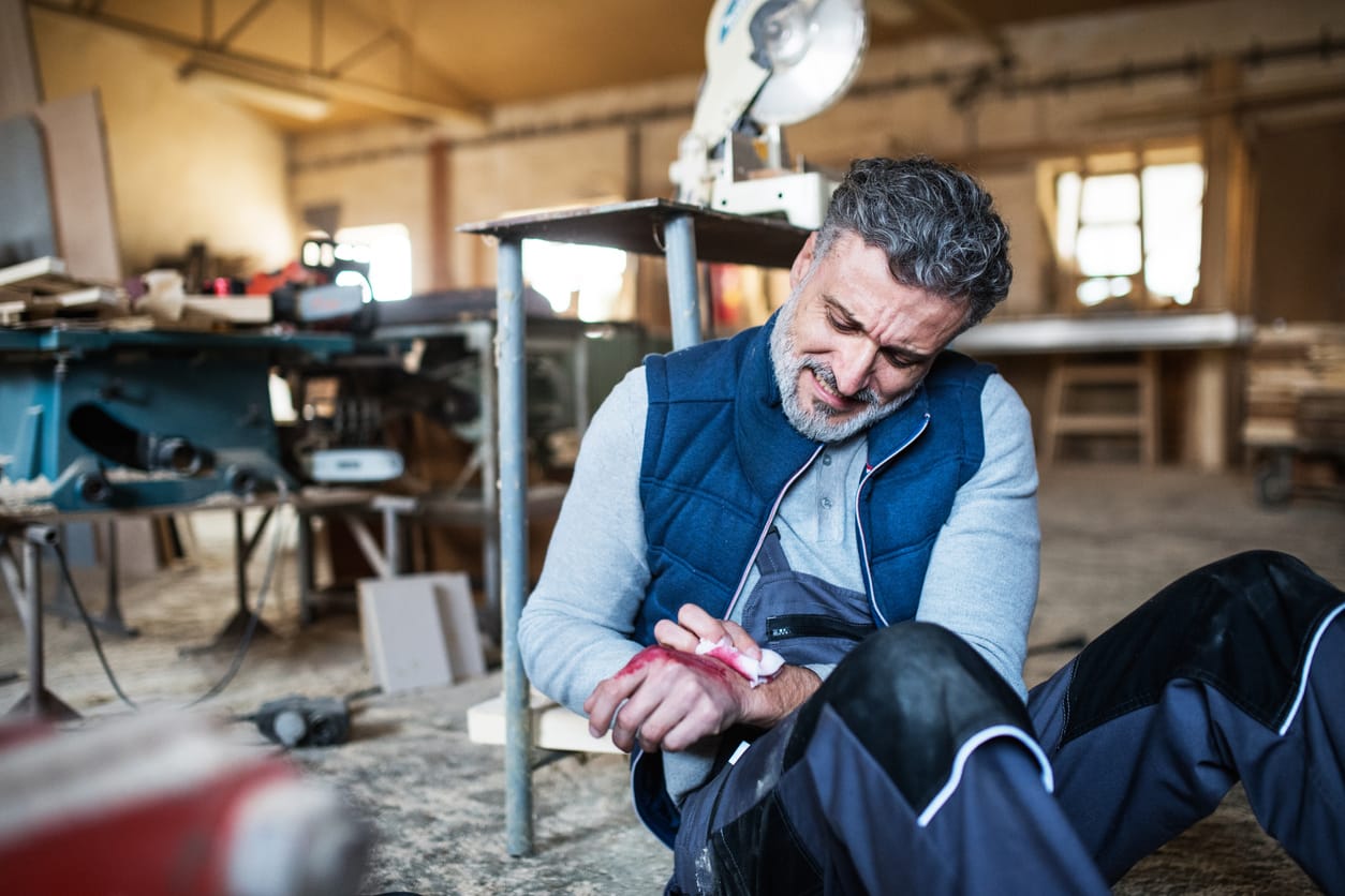older man in workshop sitting on floor with injured hand