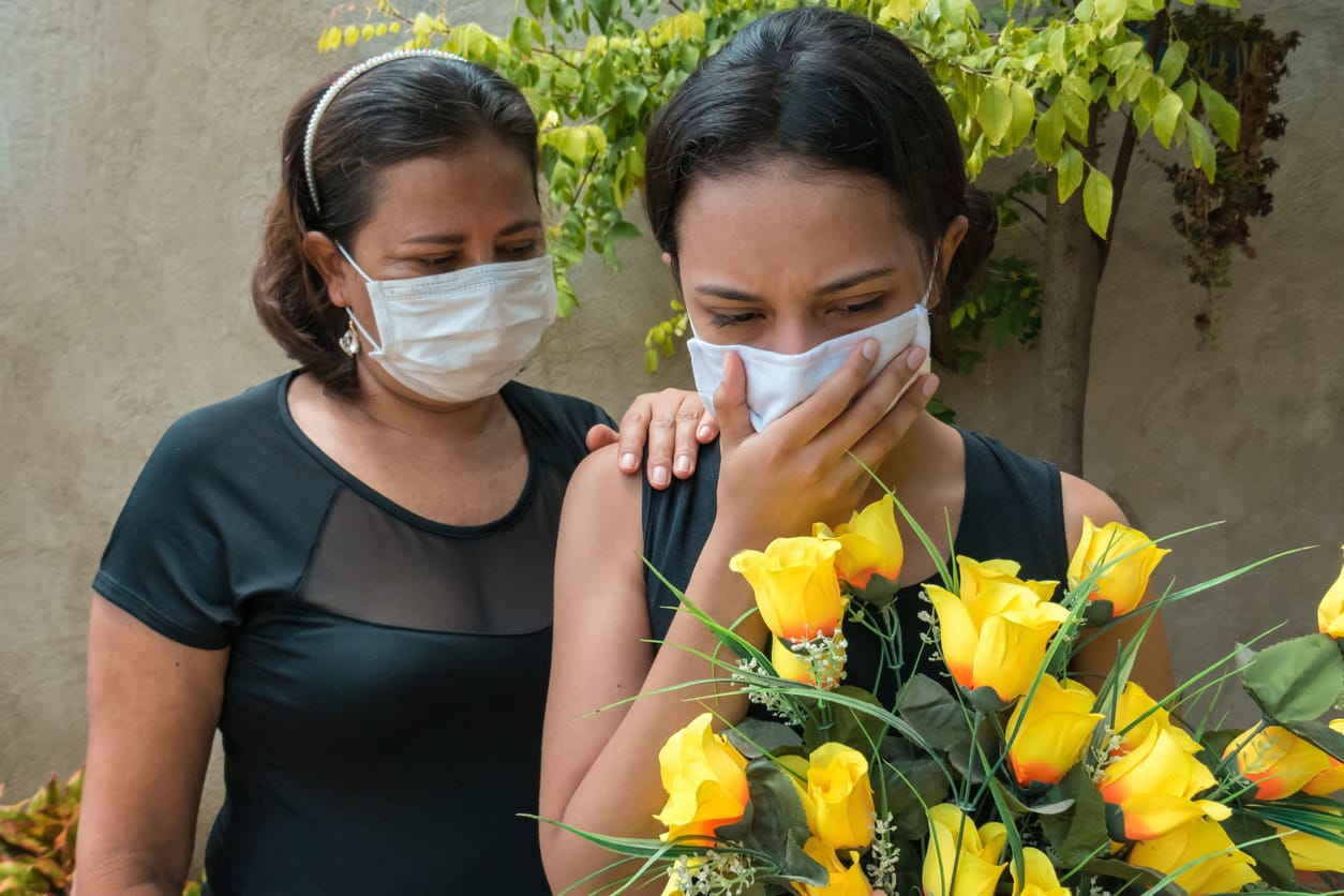 two women wearing black and masks holding flowers at a cemetery