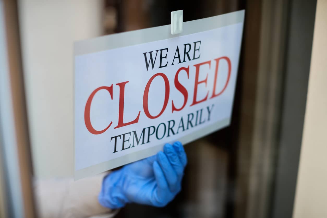 a gloved hand putting up a temporarily closed sign on a business door