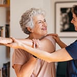 Caregiver helping senior stretch shoulder before performing exercises