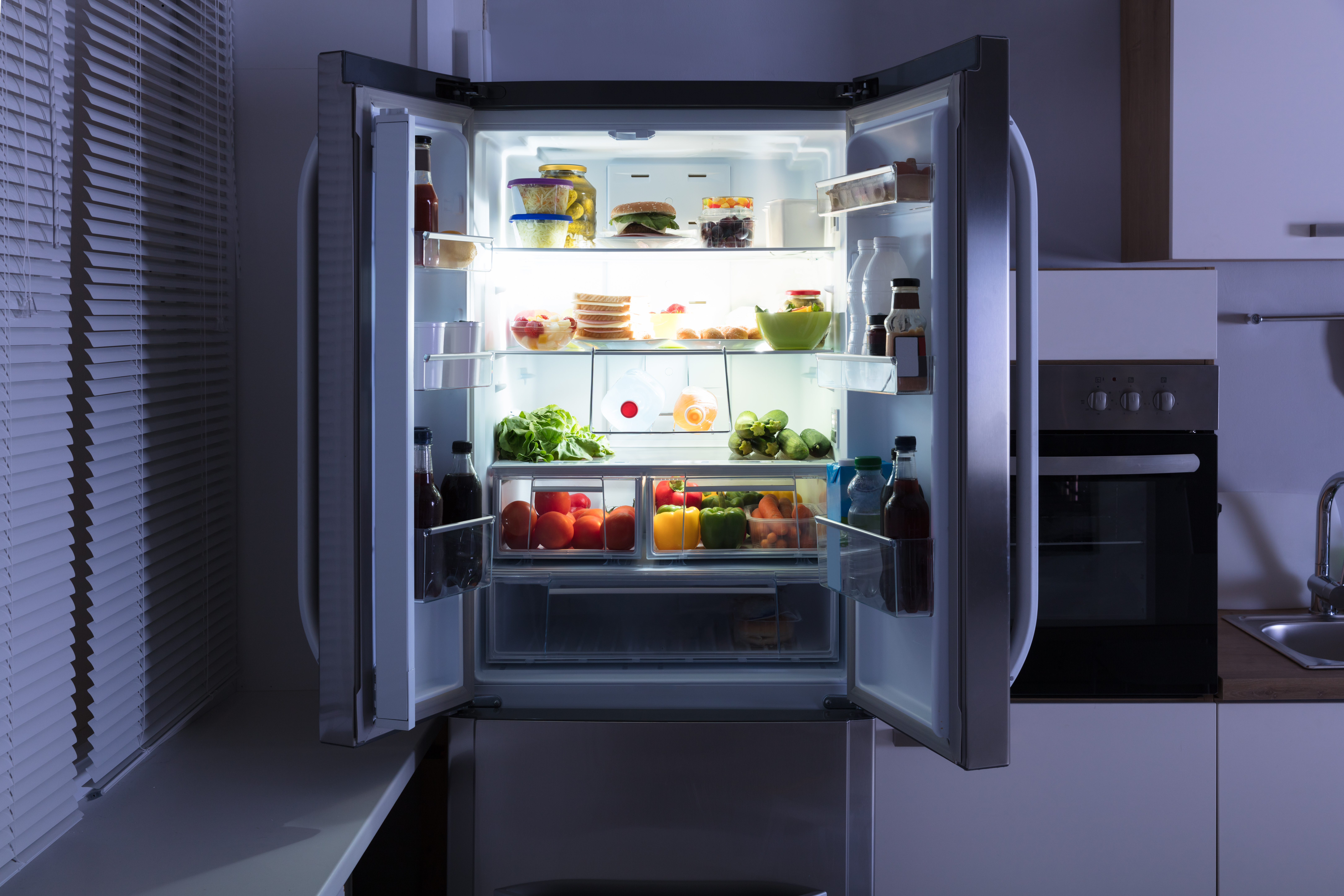 An open refrigerator in a dark kitchen, powered by a Generac Guardian 18Kw backup home generator.