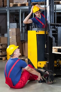 construction worker sitting on ground trying to release his foot from under a forklift