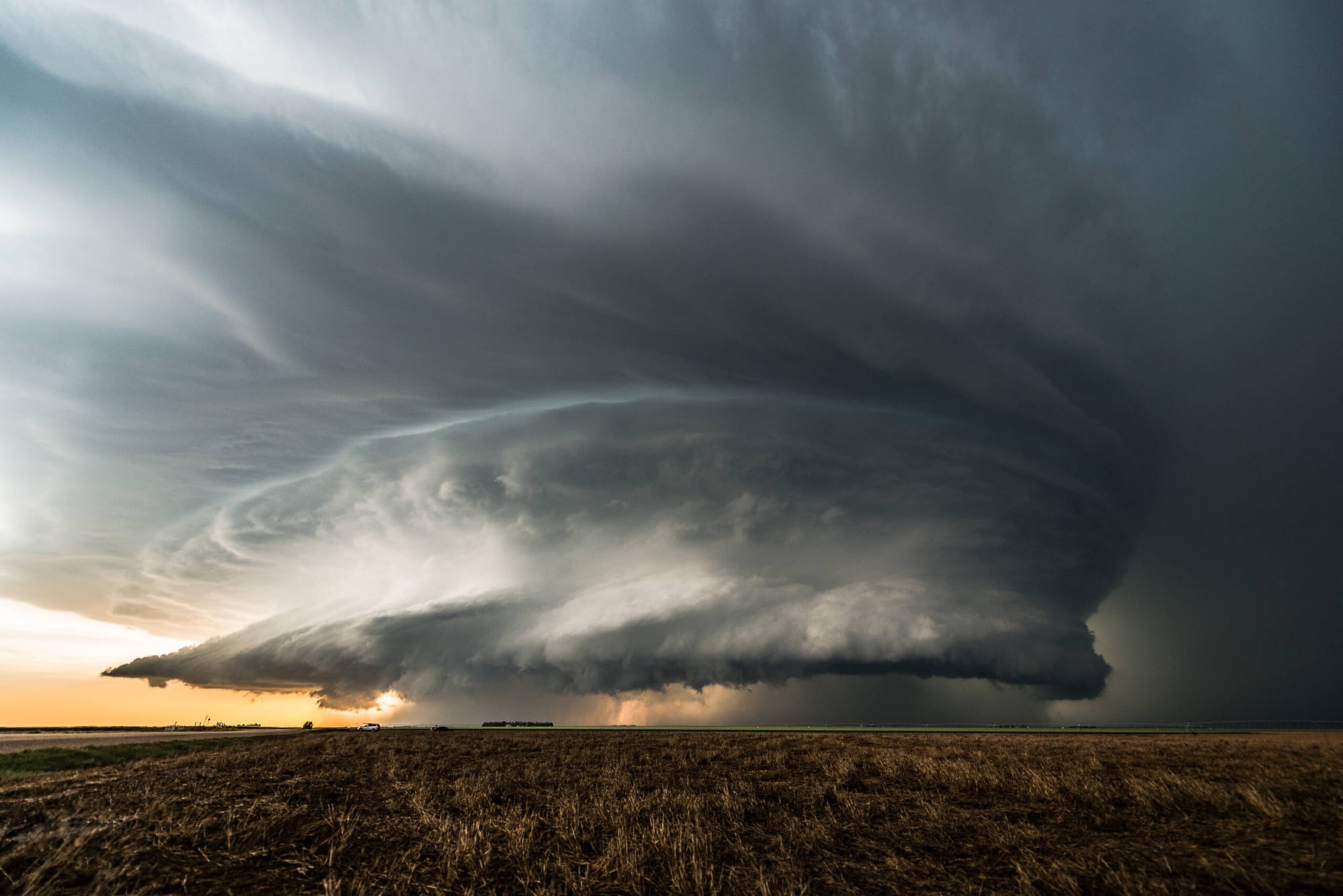 A supercell tornado about to touch down over a large field at dusk.