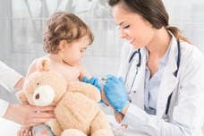 Pediatrician administering vaccine to child holding teddy bear