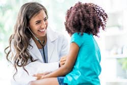 Pediatrician smiling at child while listening to heartbeat