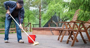 Homeowner cleaning wooden deck with broom and bucket