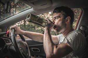 man in the driver’s seat of a car drinking out of a wine bottle