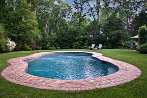 Heated gunite pool surrounded by brick patio showcases beautifully landscaped backyard