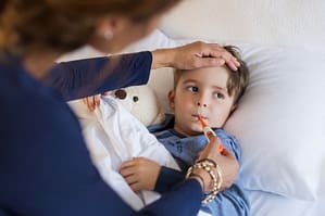 Sick Boy With Thermometer Laying In Bed With Mother's Hand on Forehead