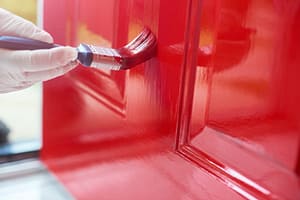 A person applies bright red paint to an exterior door