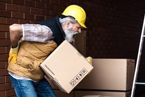 worker lifting a box and holding his back with a pained expression