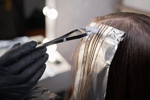 Close-up of strands of hair on special sheet of foil while hairdresser applies hair dye with brush