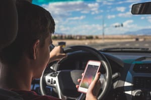 a young driver looking at his cell phone while driving 