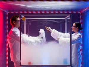 : a man and a woman mixing chemicals in a steamy sterile chamber labeled as biohazardous