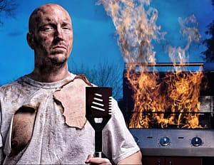 man with burnt shirt standing in front of a grill that’s on fire
