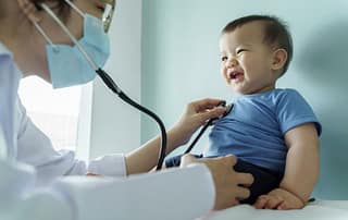 Pediatrician listening to a laughing baby’s heart with a stethoscope
