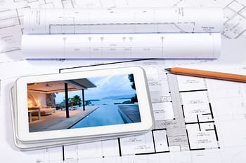 Digital tablet with photo of house and pool on top of blueprints 