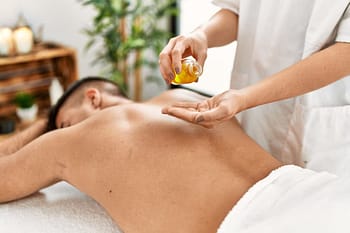Client lies on stomach while massage therapist applies raindrop therapy essential oils to spine