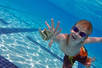 Young swimmer reaching for dollar bill underwater 