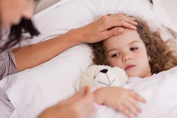 Pediatric patient lies in bed with stuffed toy as parent reads thermometer