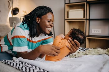 Young mom playing with baby on bed at home 