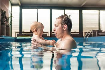 Two family members learn how to swim in private indoor pool with large windows