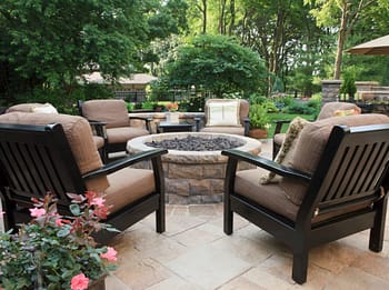 Patio chairs situated around fire pit with landscaping scattered throughout property 