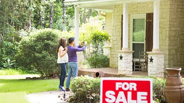 “For sale” sign in front of a home, with house flippers taking a picture