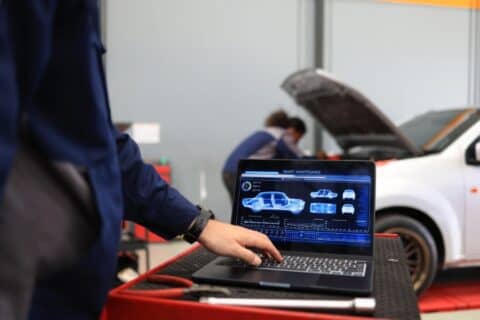 Auto mechanic working on car using assistance technology on laptop