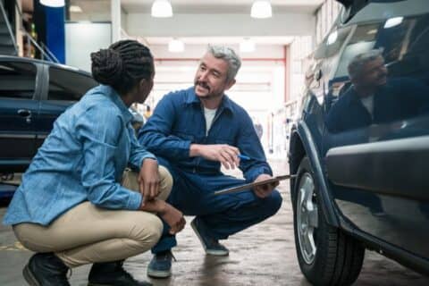 Car mechanic checking car wheel in auto repair shop and talking with customer