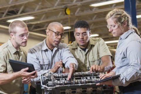 A technical college instructor shows three students how to repair a gasoline engine