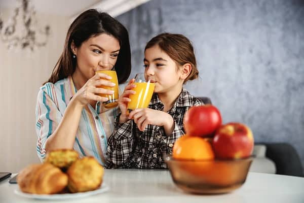 Mother And Daughter Having A Healthy Breakfast. They Are Drinking Orange Juice.