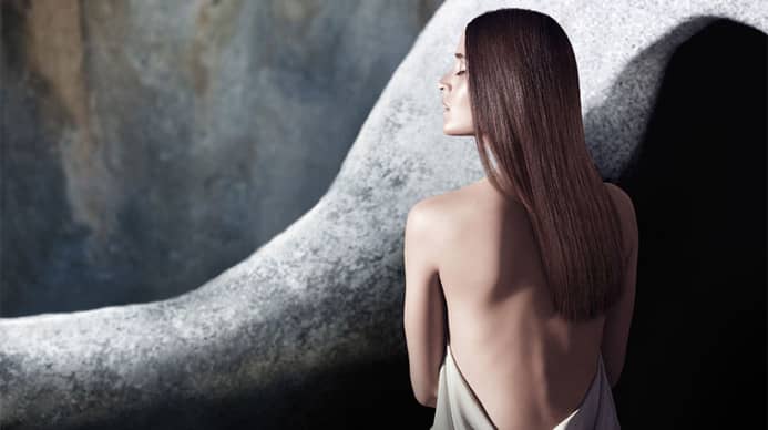 Aveda model with bare back witting in a natural setting