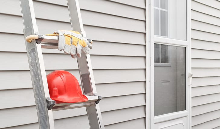 Red hard hat and work gloves on a ladder leaning against a house