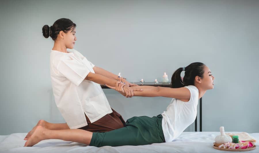 Thai massage practitioner stretching client's arms backward