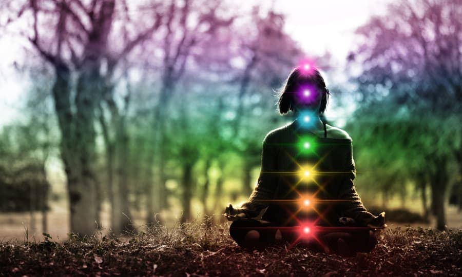 Silhouette of a person sitting outside in lotus pose with glowing chakras