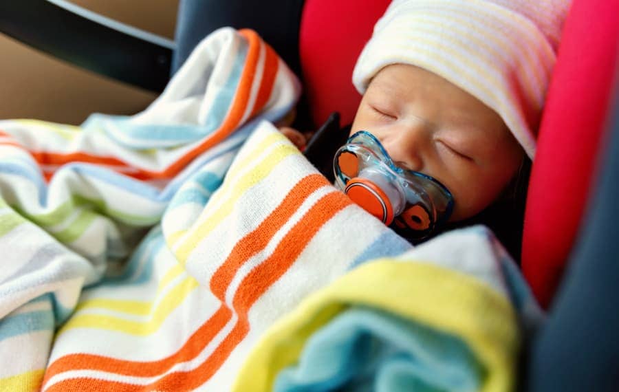 Newborn baby with pacifier swaddled and strapped into car seat