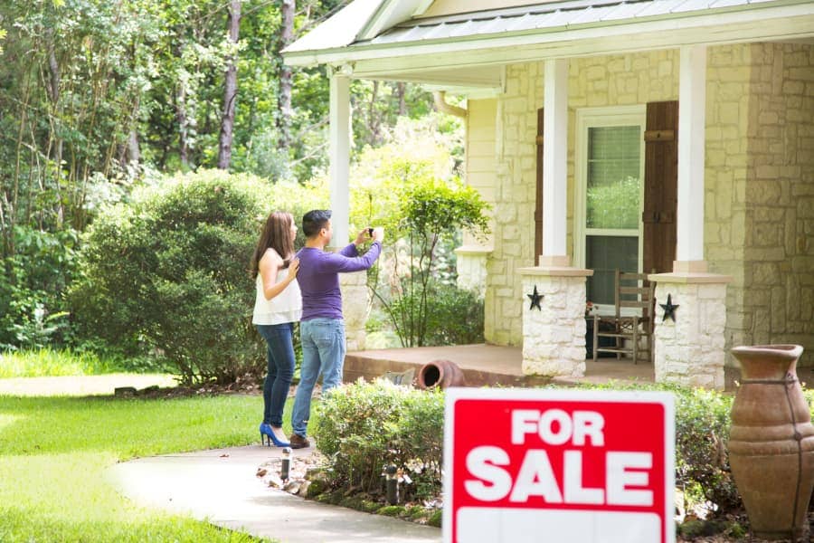 “For sale” sign in front of a home, with house flippers taking a picture