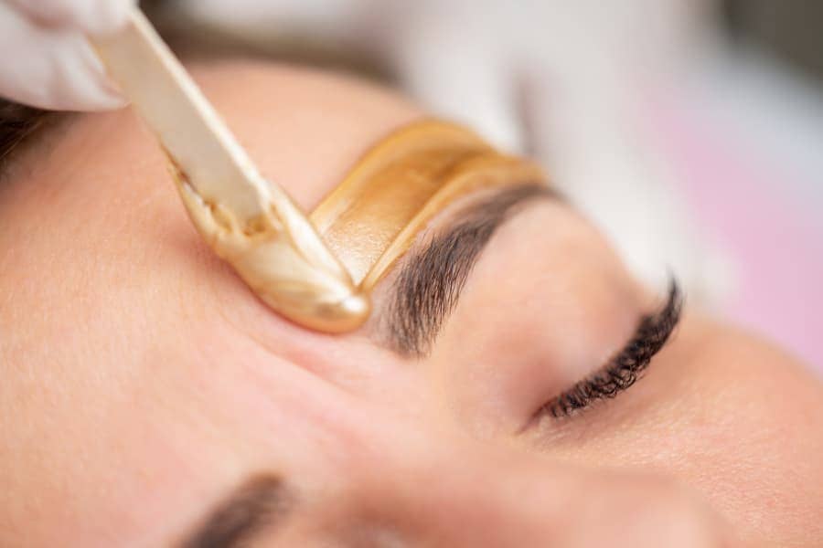 Technician applying gold-colored wax above eyebrows