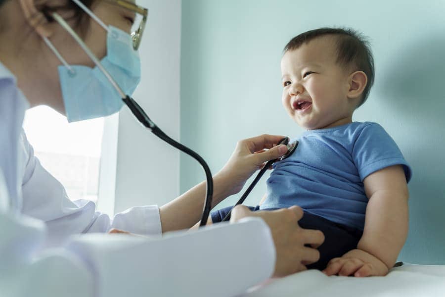 Pediatrician listening to a laughing baby’s heart with a stethoscope