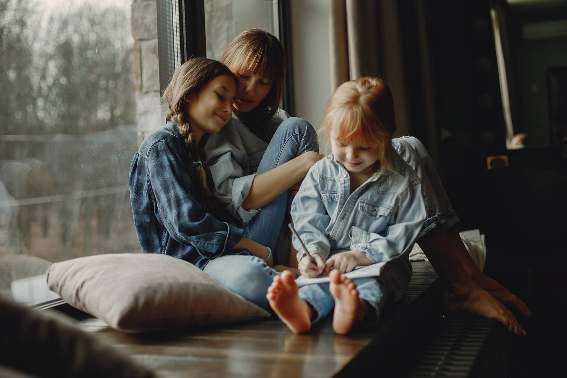 Mom and two daughters sitting in front of a large window.